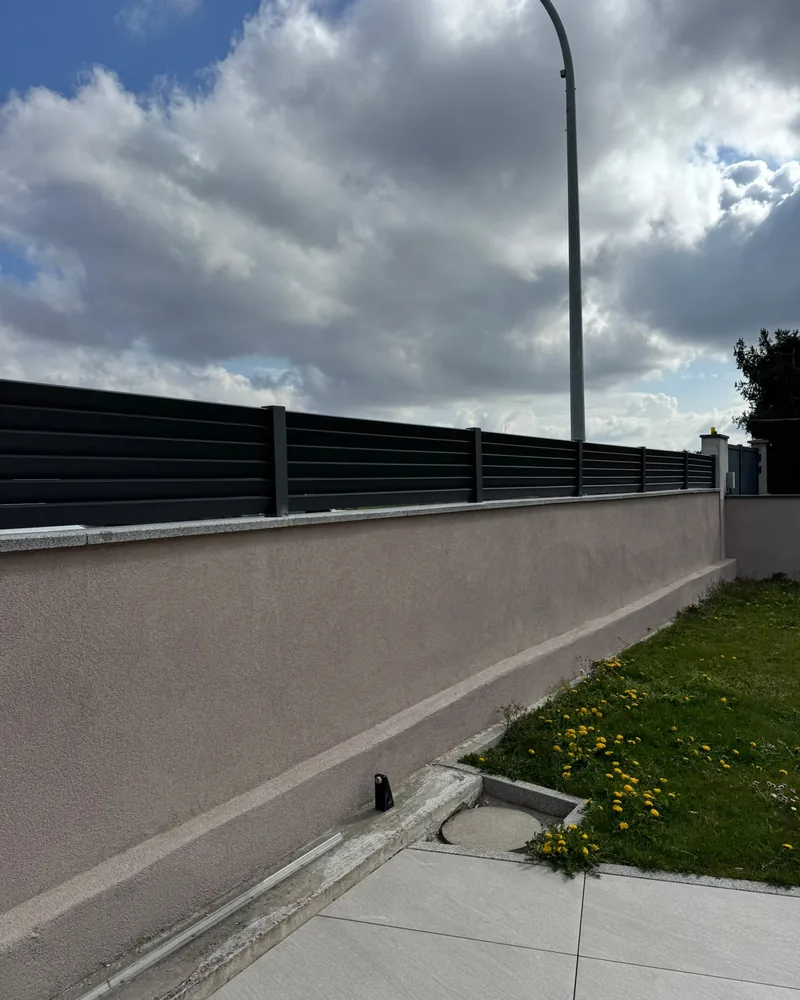 Clôture à lames horizontales anthracite posée sur un muret crépi, au bord d’une terrasse — photo de chantier