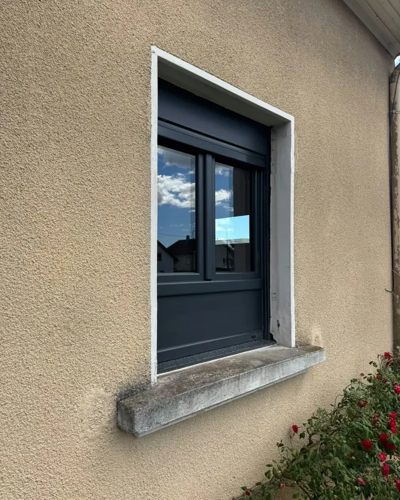 Fenêtre anthracite avec volet roulant dans une façade crépie, après la pose — photo de chantier